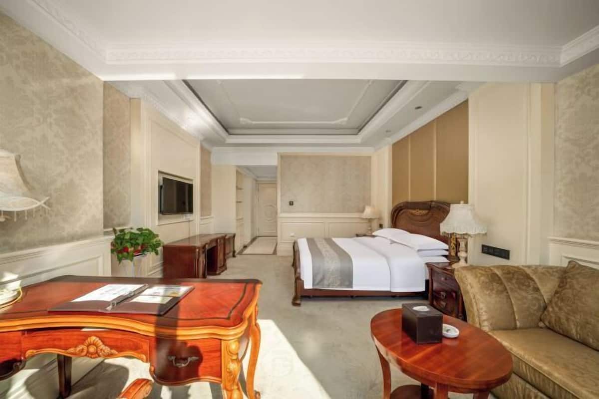 Habitación de hotel con una cama grande, un escritorio de madera, un sofá y un televisor.