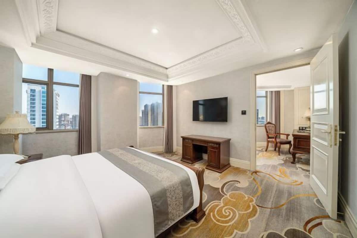 Habitación de hotel con una cama grande, un escritorio, televisión y vistas a la ciudad a través de las ventanas.
