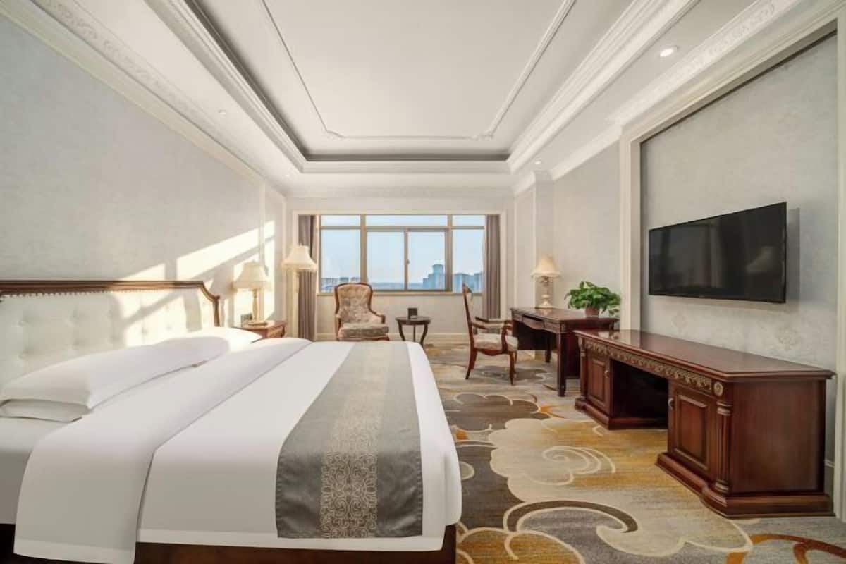 Habitación de hotel con una cama grande, un escritorio, una silla, un televisor y vistas a la ciudad.