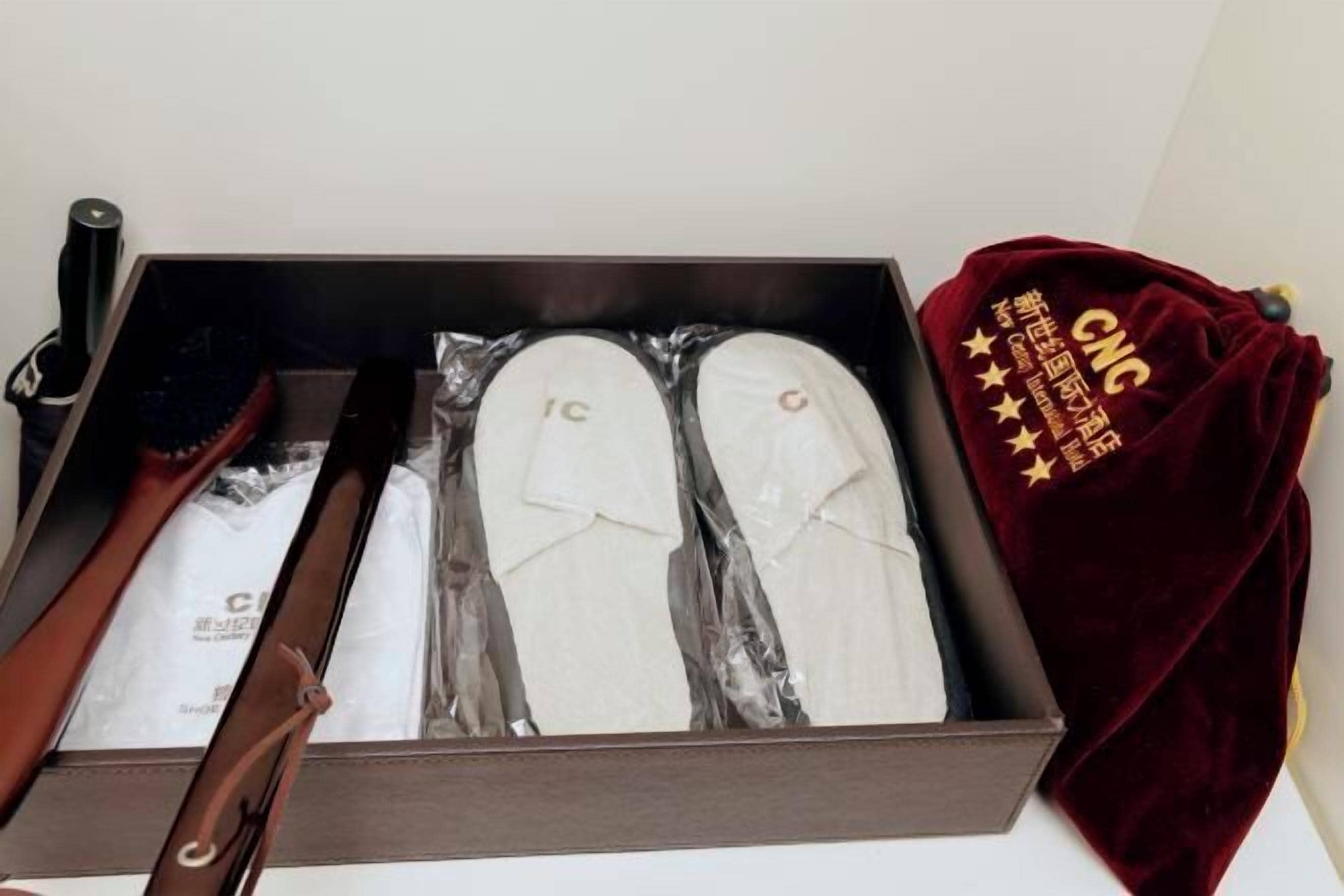 A box containing a pair of white shoes, a black brush, and a red cloth with text.