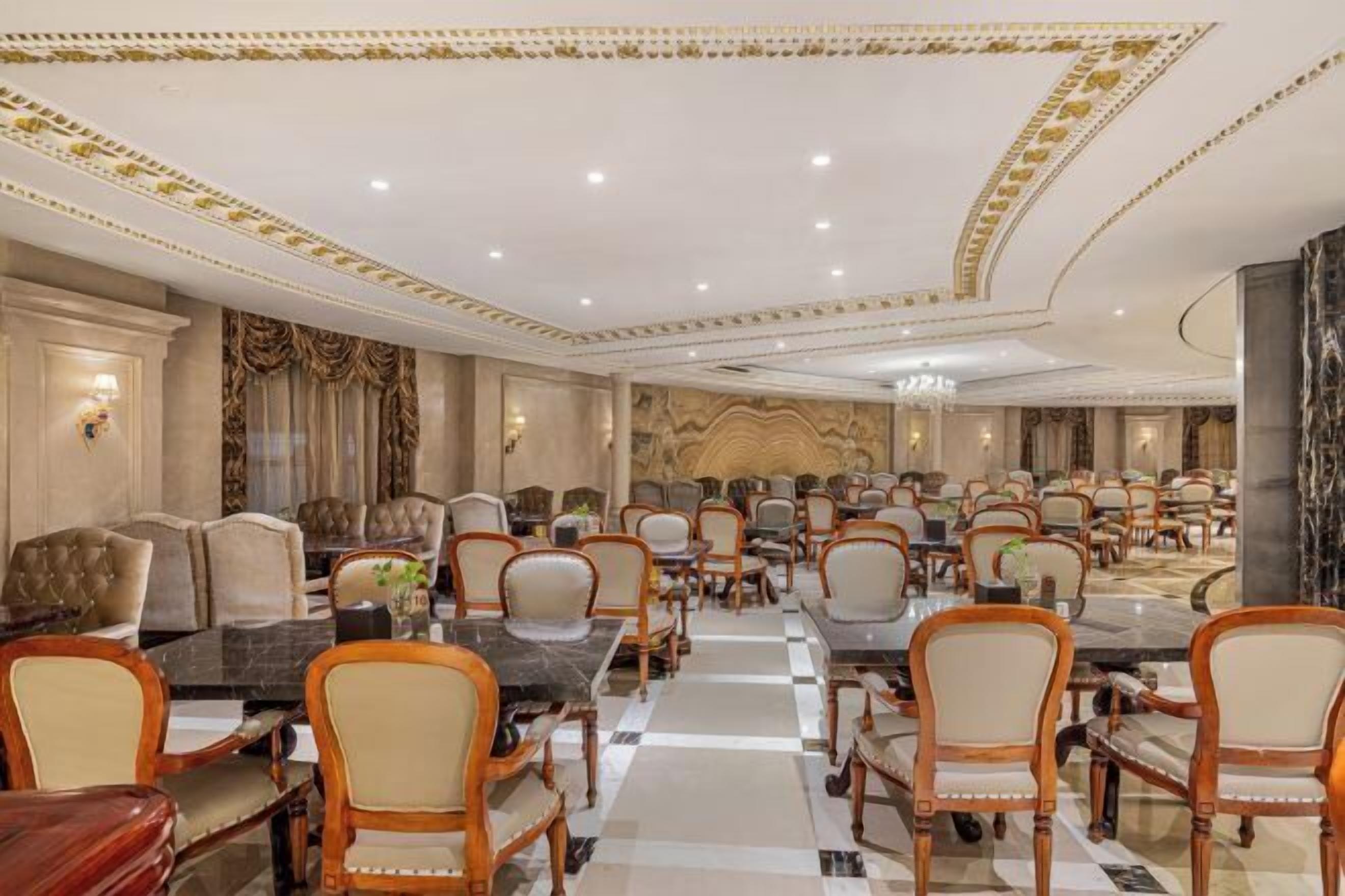 A spacious banquet hall with multiple round tables and chairs, elegant chandeliers, and a marble floor.