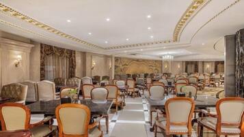 A spacious banquet hall with multiple round tables and chairs, elegant chandeliers, and a marble floor.