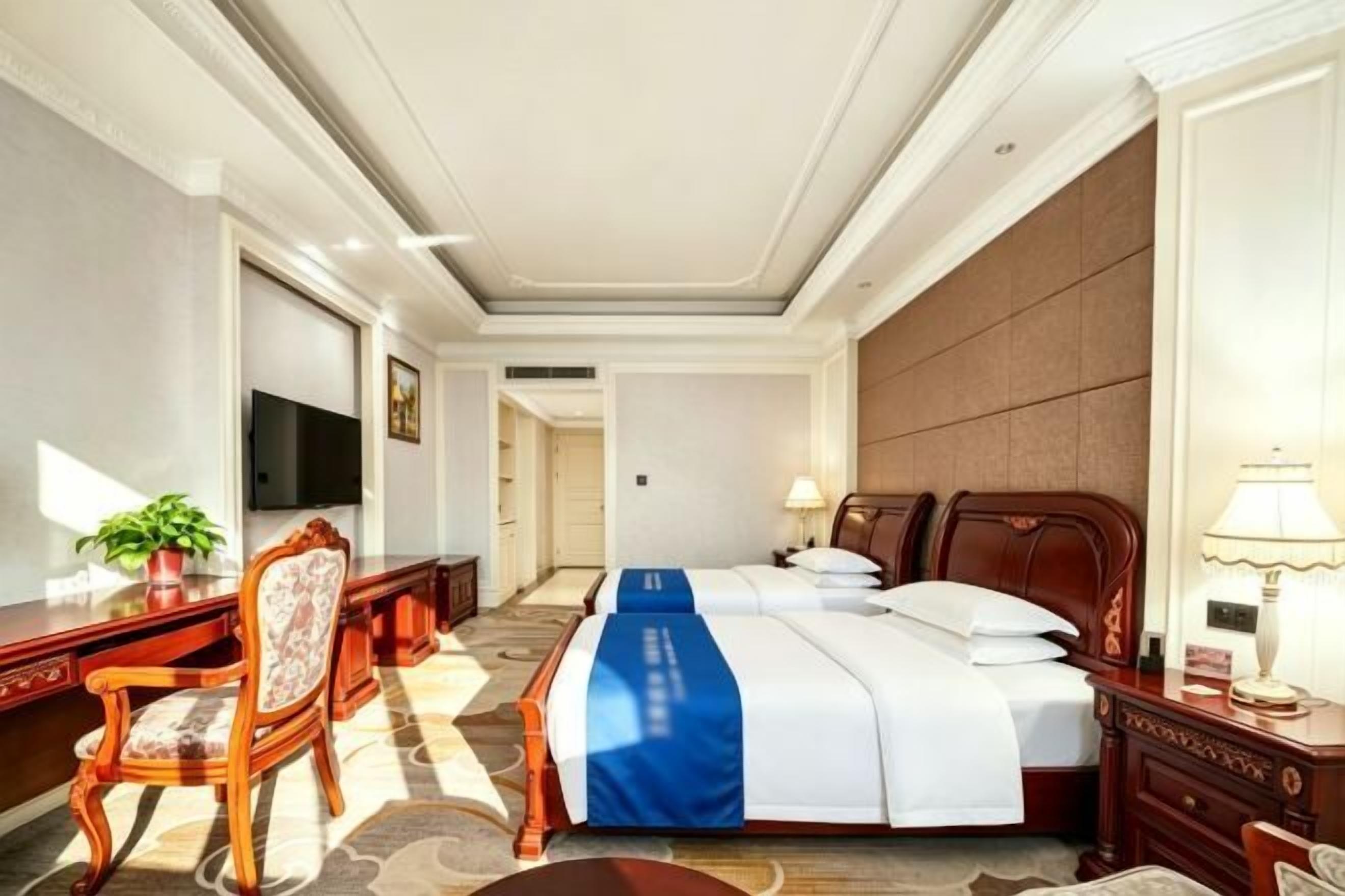 Habitación de hotel con cama, escritorio, silla, televisión y lámpara.