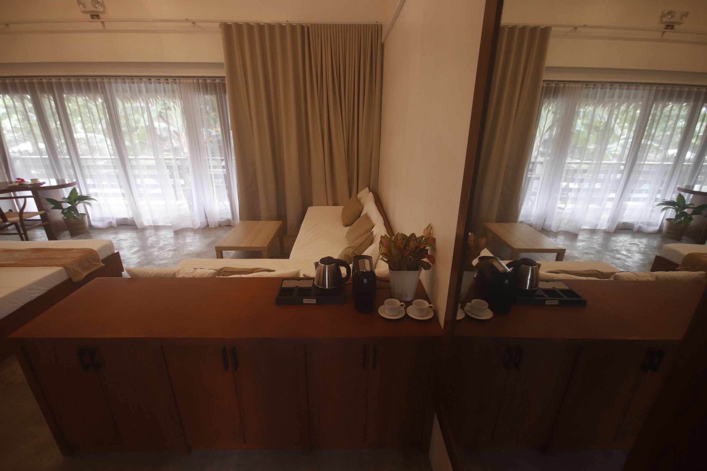 A hotel room with a bed, a sitting area with a table, and a large window with curtains.
