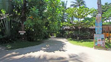 A narrow road flanked by lush greenery and a thatched-roof structure. A 'No Parking' sign is visible on the left.