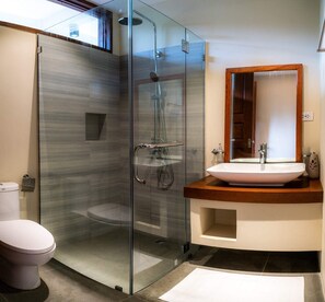A modern bathroom with a glass-enclosed shower, a white sink with a wooden countertop, and a large mirror. - The Henry Resort at Kermit Siargao (General Luna)