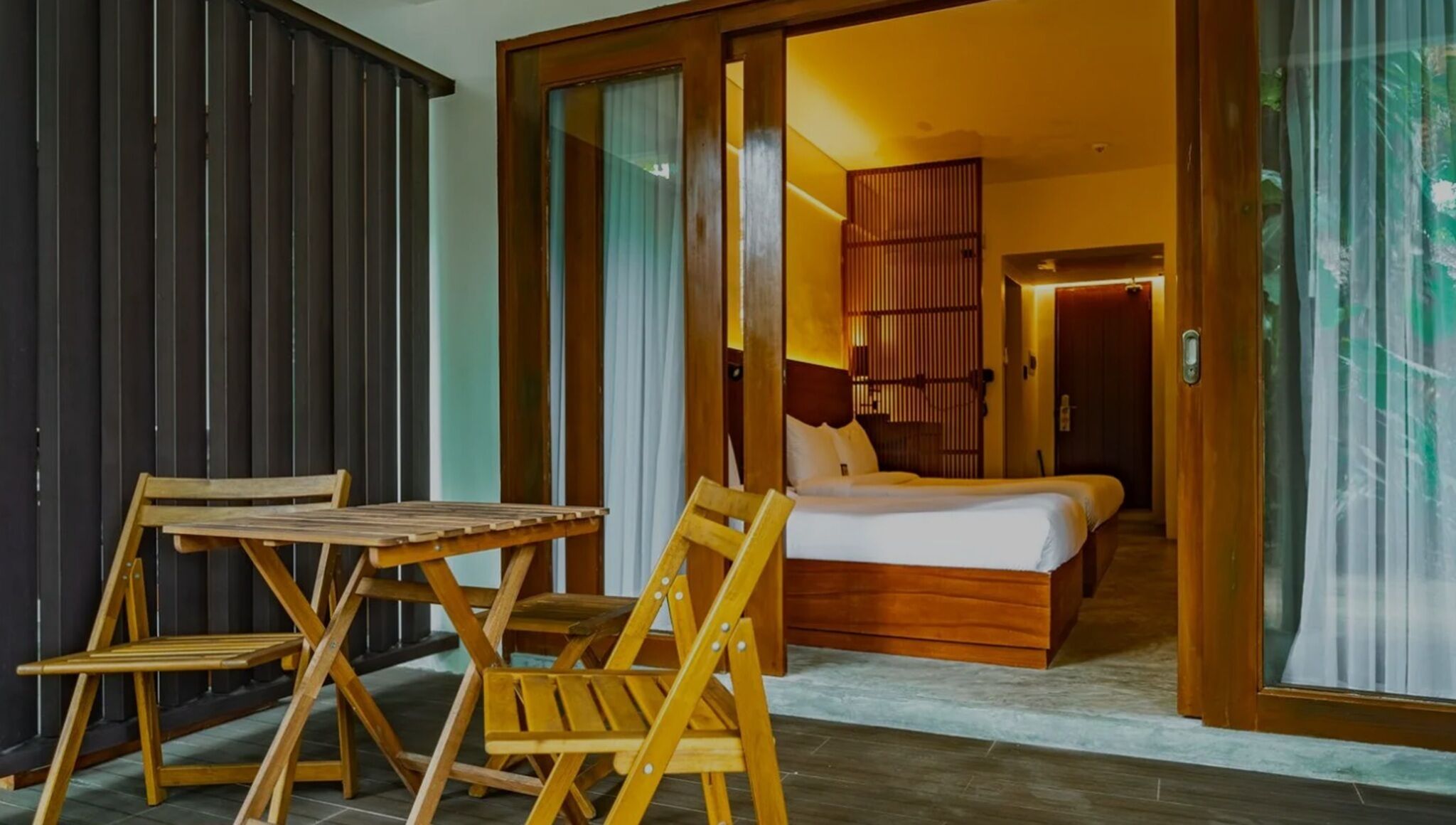 Una habitación con una cama, una mesa de madera y sillas, y vistas a un balcón con barandilla de madera.