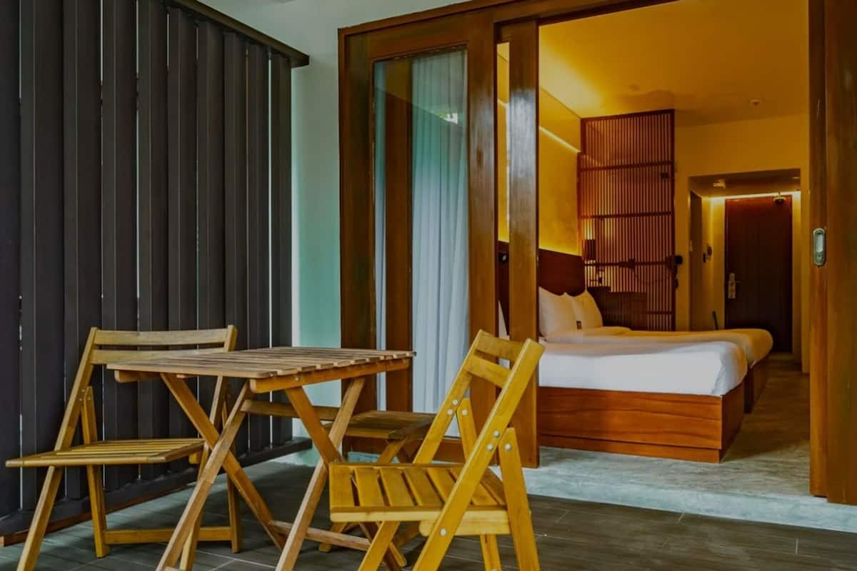 Une pièce comprenant un lit, une table en bois et des chaises, et donnant sur un balcon doté d’une balustrade en bois.