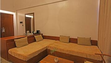 A modern hotel room with a large L-shaped sofa, a small wooden coffee table, and a potted plant.