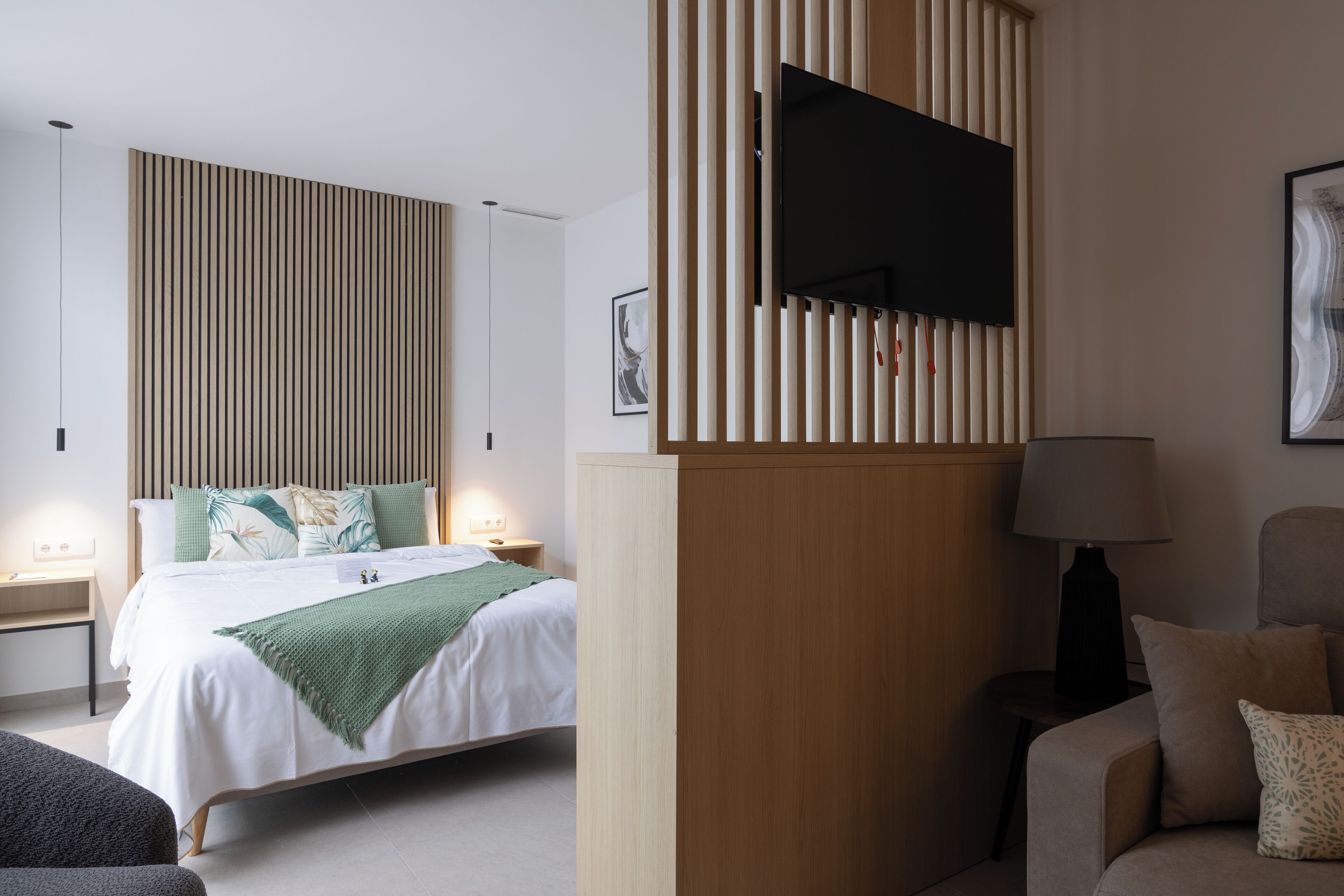 Una habitación de hotel moderna con cama, mesitas de noche, televisor, lámpara y sofá.