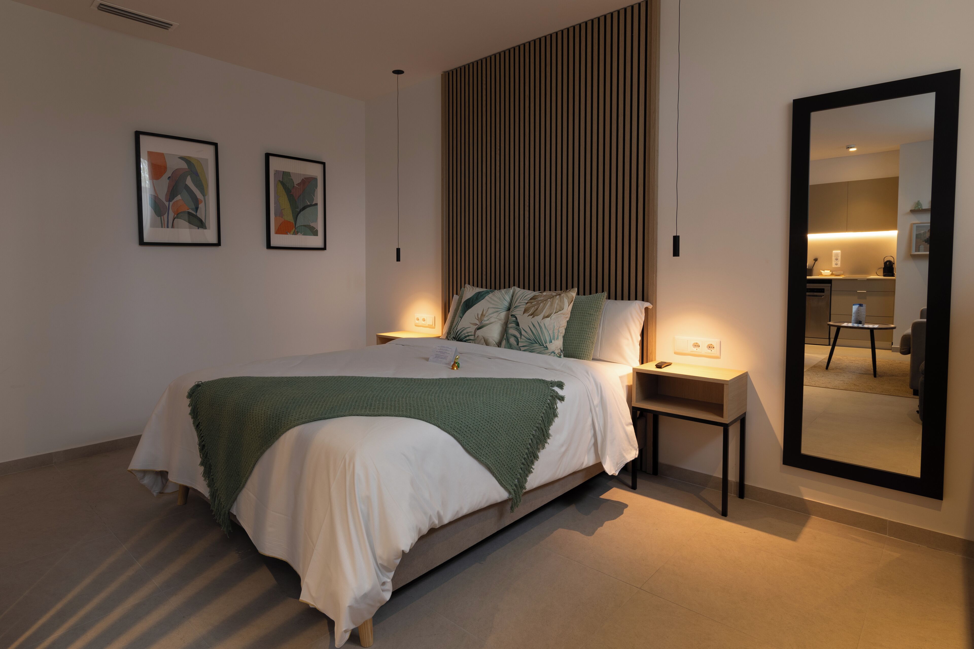 A modern bedroom with a large bed, bedside tables, a mirror, and abstract wall art.