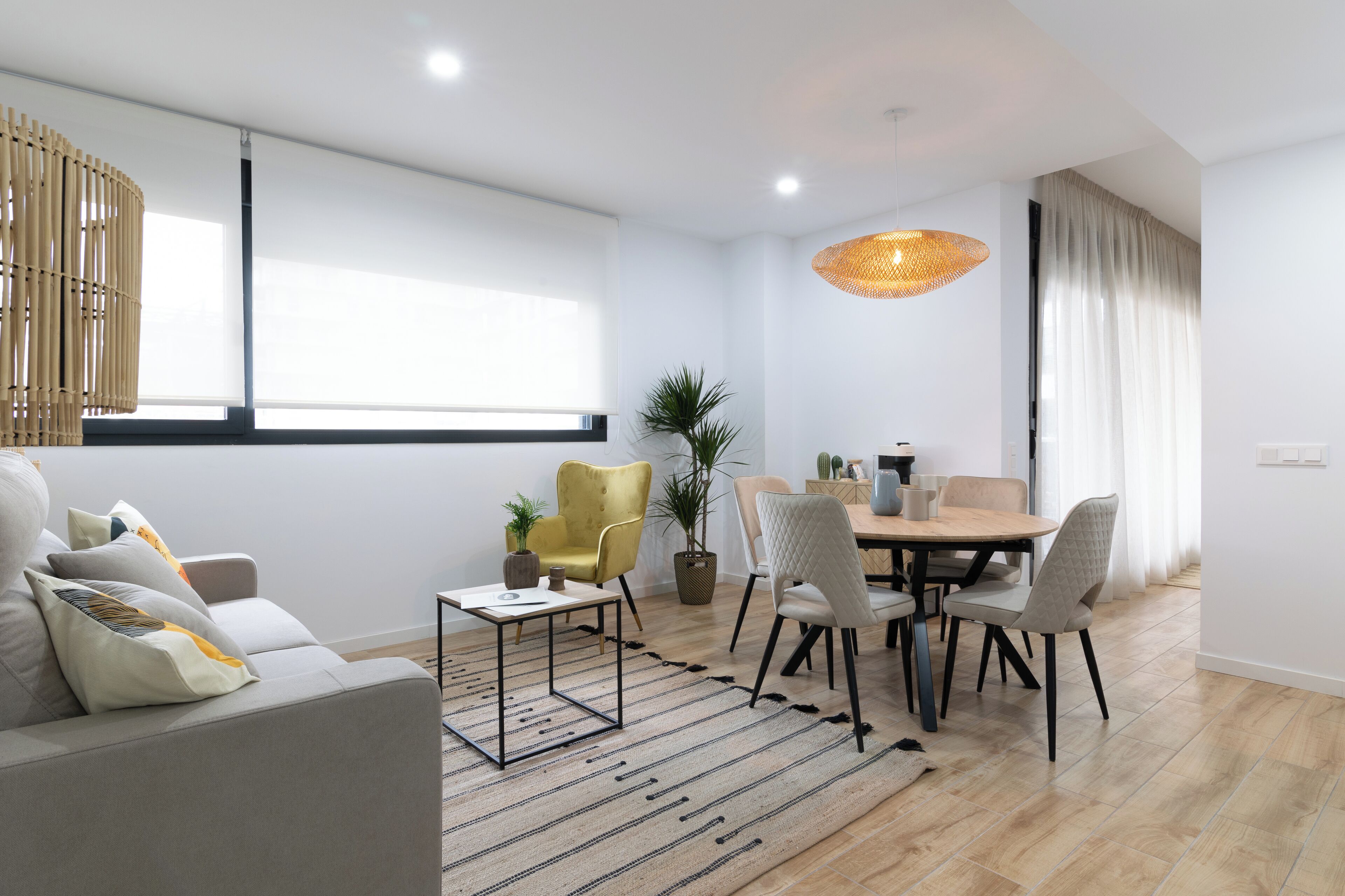 Una sala de estar moderna con un sofá, una mesa de comedor con sillas, una mesa de centro y una lámpara colgante.