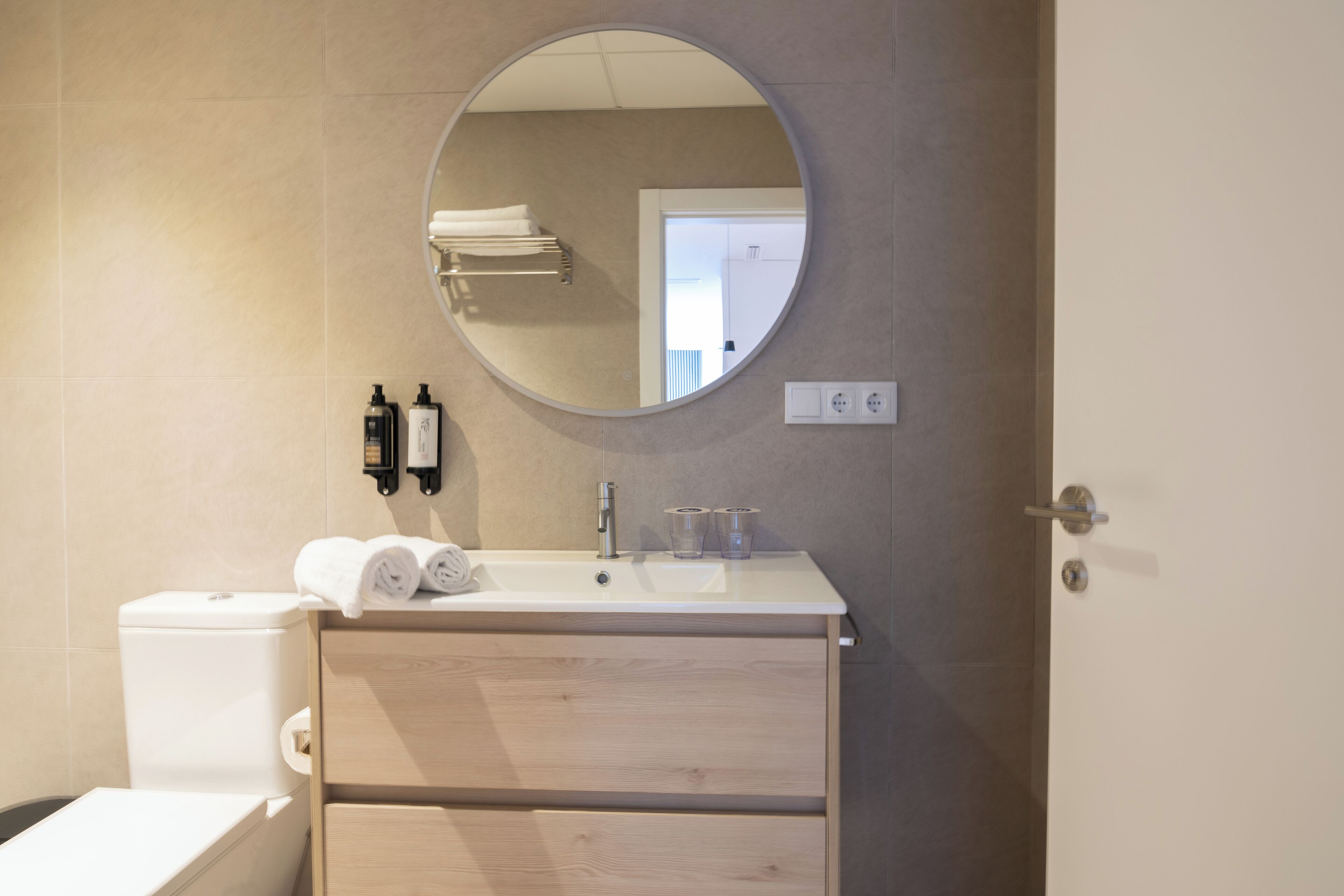 Une salle de bain moderne avec des toilettes, un lavabo et un miroir. On trouve des serviettes et des articles de toilette sur le lavabo.