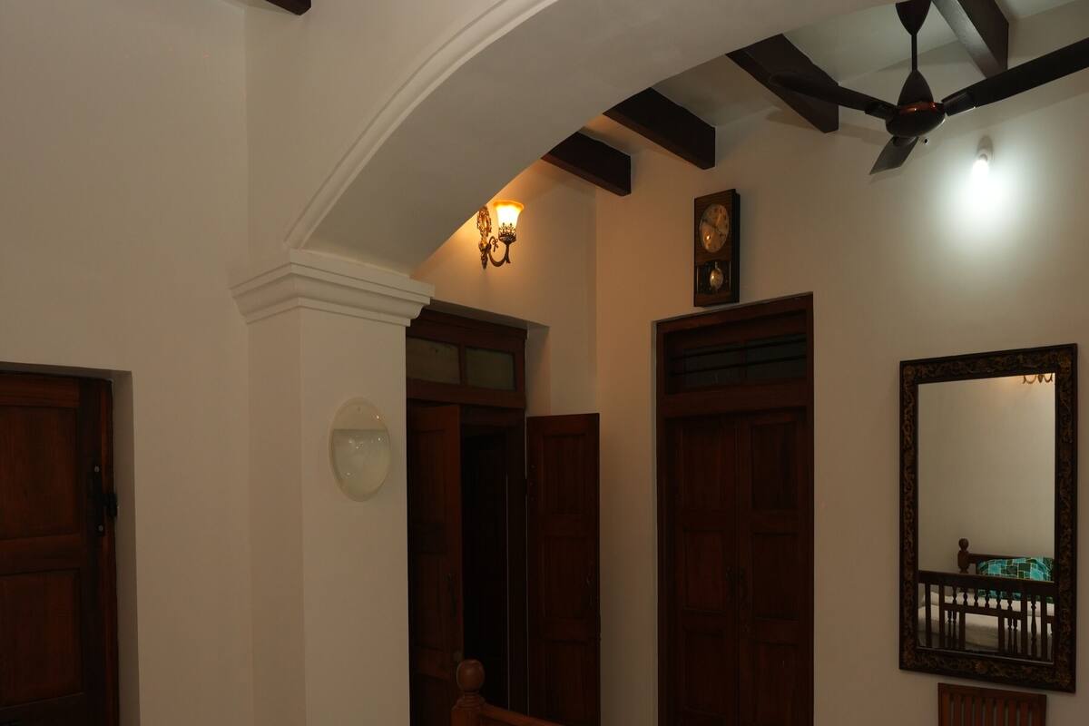 A bedroom with a bed, wooden headboard, a ceiling fan, a wall clock, and a mirror.