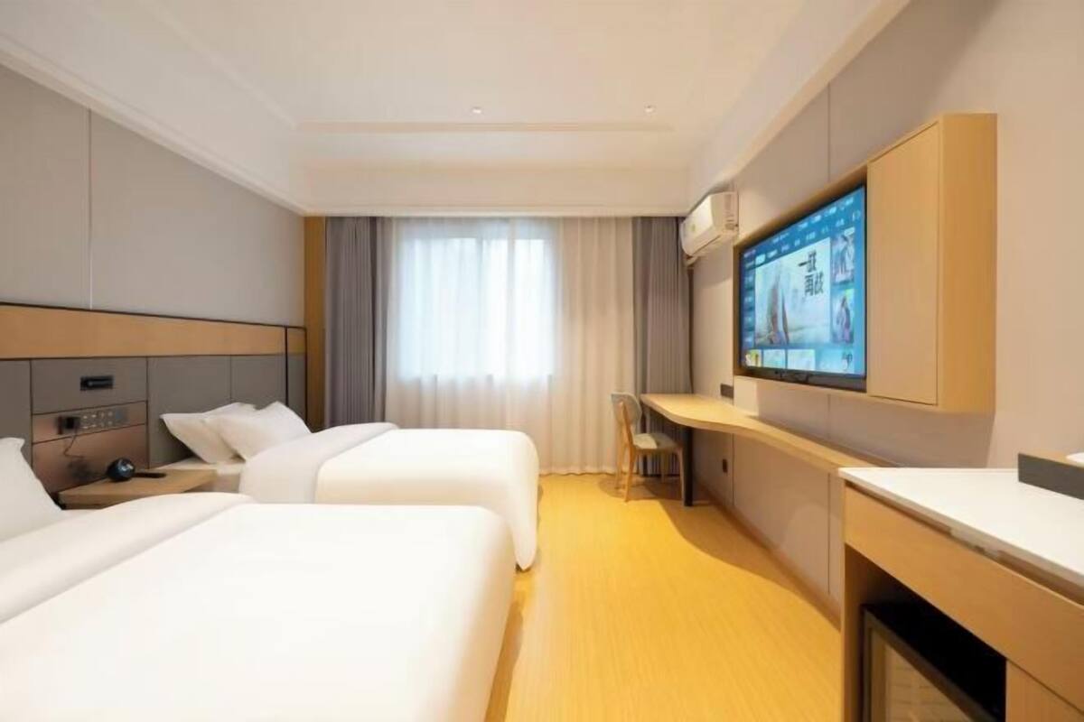 Une chambre d’hôtel avec deux lits, un bureau, une télévision et une fenêtre avec des rideaux.