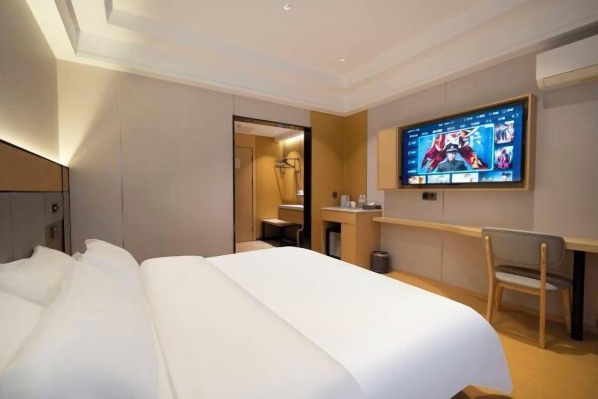 Une chambre d’hôtel avec un grand lit, un bureau, une chaise, une télévision et une salle de bain visible à travers une porte ouverte.