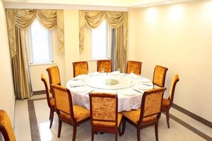 A round table with chairs, set for dining, in a room with windows and curtains.