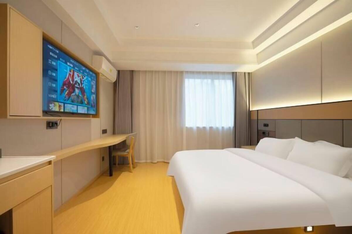 Une chambre d’hôtel avec un lit, un bureau, un téléviseur fixé au mur et une fenêtre avec des rideaux.