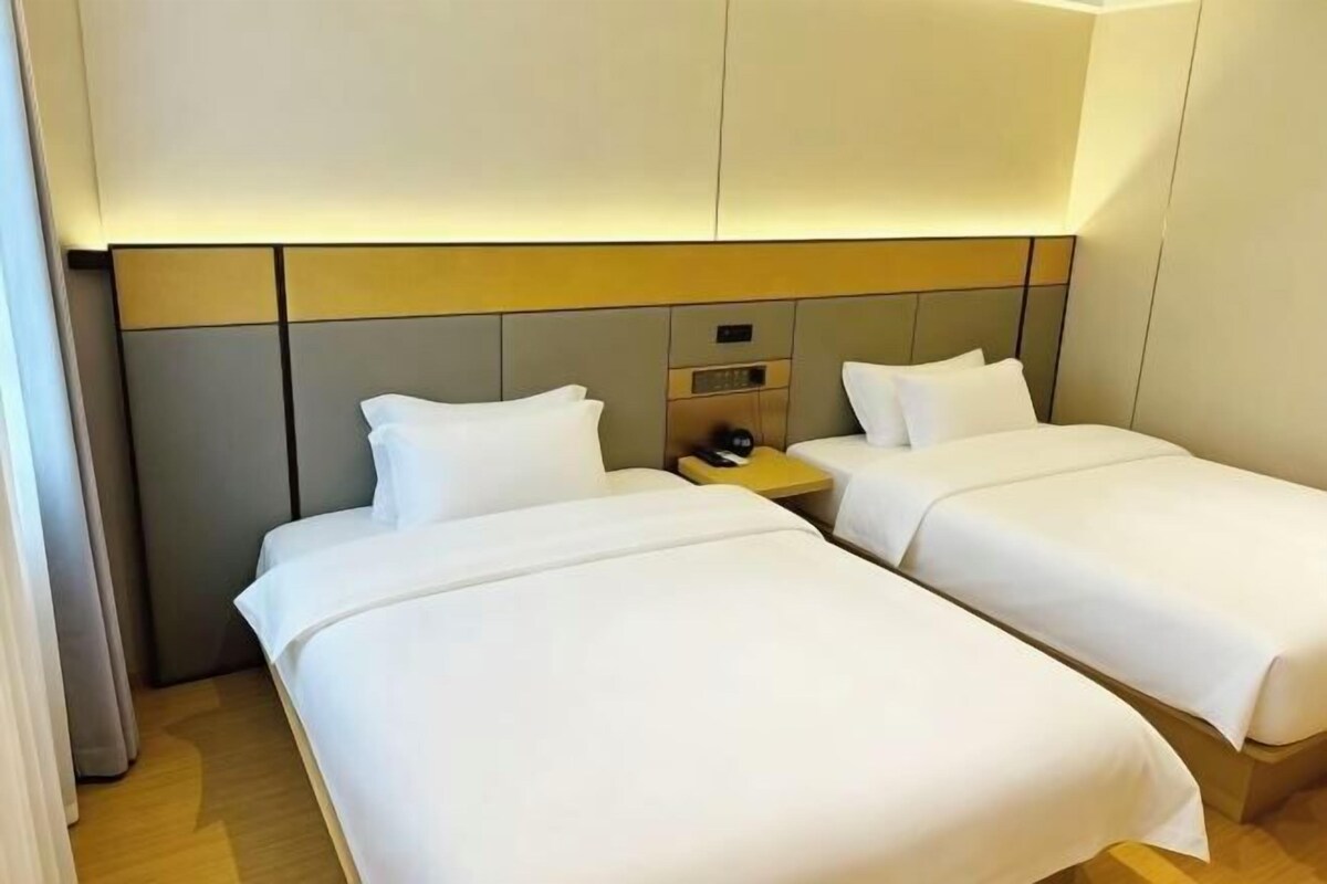 Quarto de hotel com duas camas, uma mesinha de cabeceira e cabeceira com painel de controle.