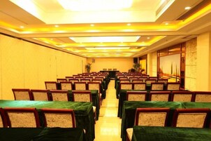 Un salón de conferencias con filas de mesas y sillas, una mesa larga al frente, y piso alfombrado.