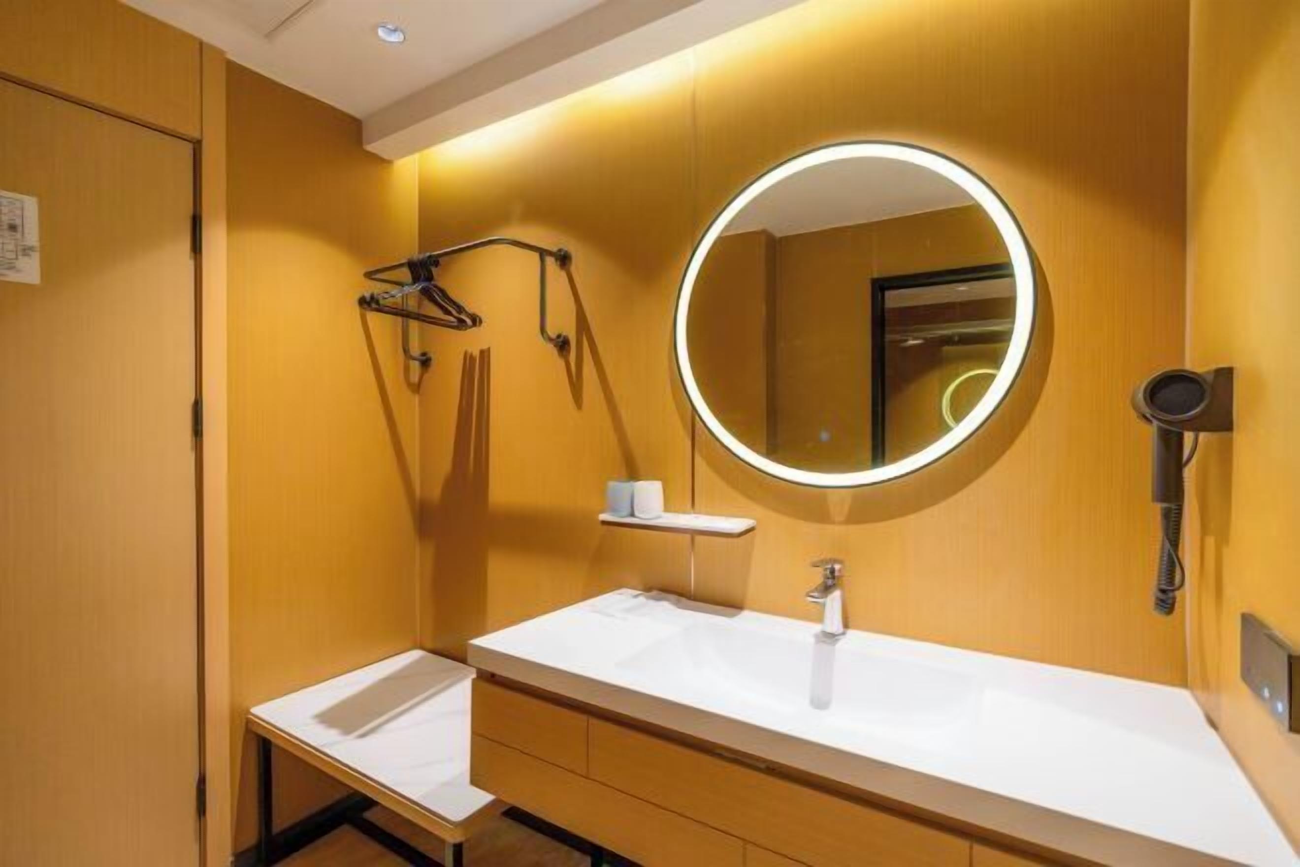 Une salle de bain avec un lavabo blanc, un miroir rond avec un éclairage intégré et un porte-serviettes.