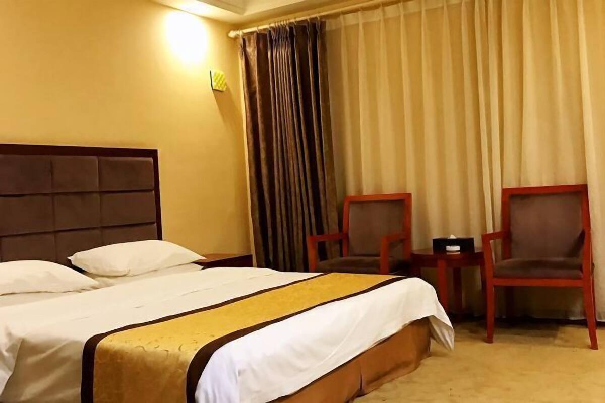 Une chambre d’hôtel avec un grand lit, deux chaises, une petite table et un rideau.