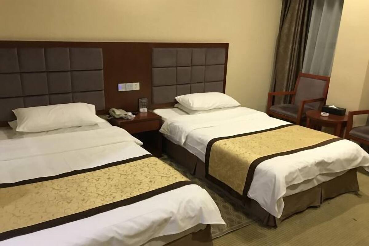 Une chambre d’hôtel avec deux lits, une table de chevet, une chaise et une fenêtre avec des rideaux.