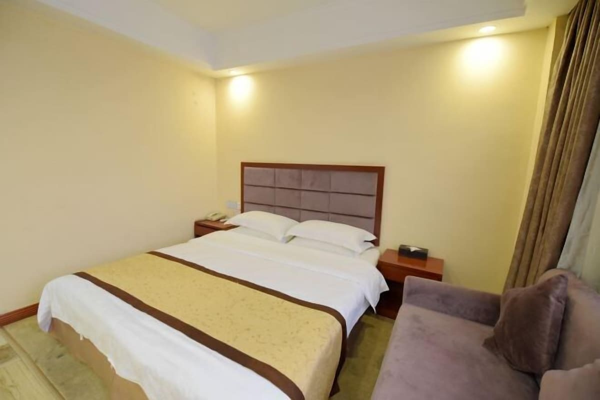 Una habitación de hotel con una cama grande, una mesita de noche con lámpara y un sofá.