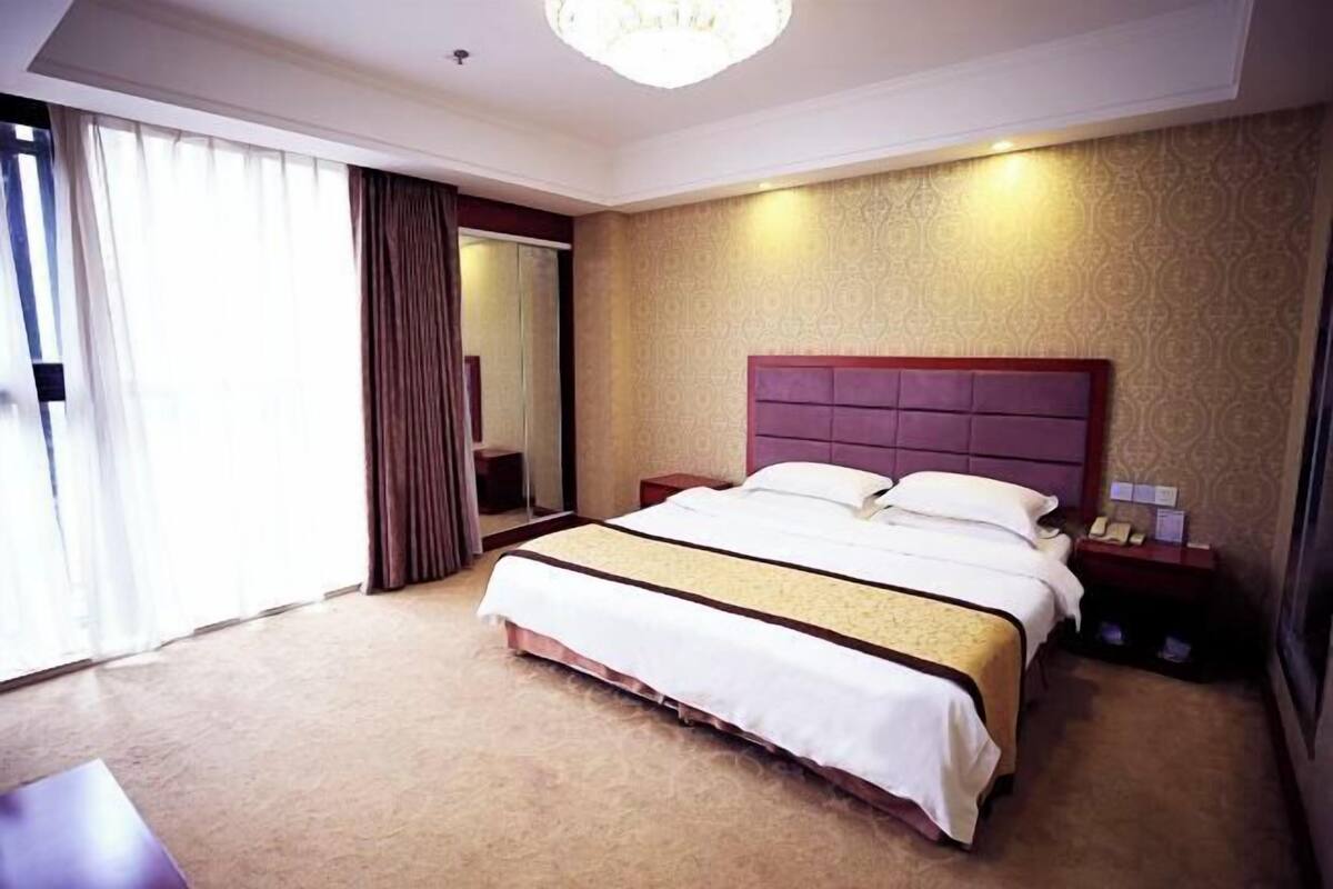 Une chambre d’hôtel avec un grand lit, une table de chevet, un miroir et un lustre.