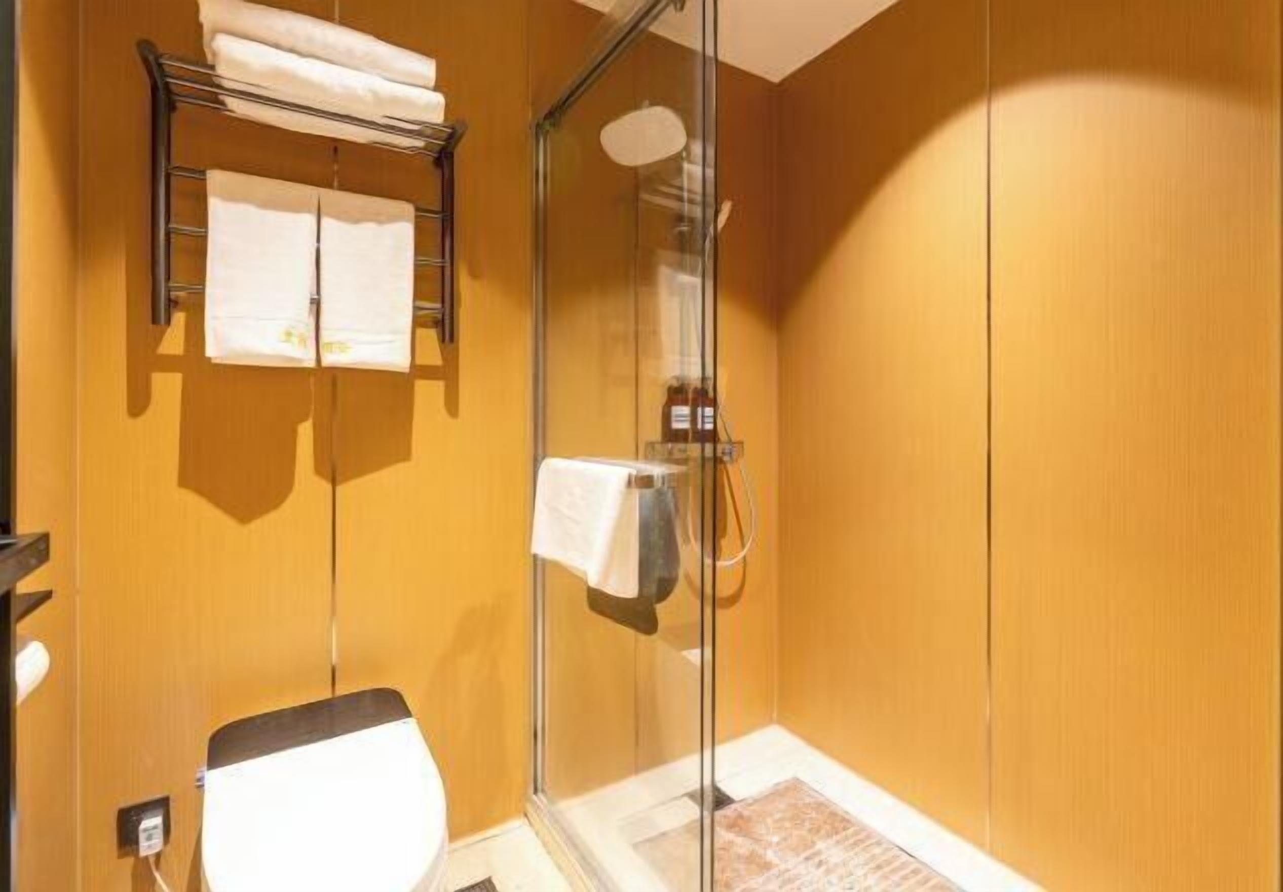 A bathroom with a glass shower enclosure, a towel rack with folded towels, and a toilet.