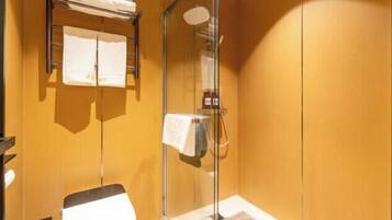 A bathroom with a glass shower enclosure, a towel rack with folded towels, and a toilet.