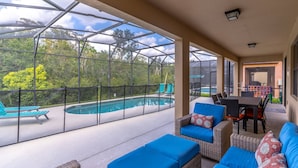 A covered outdoor area with a pool, blue cushioned seating, and a table.