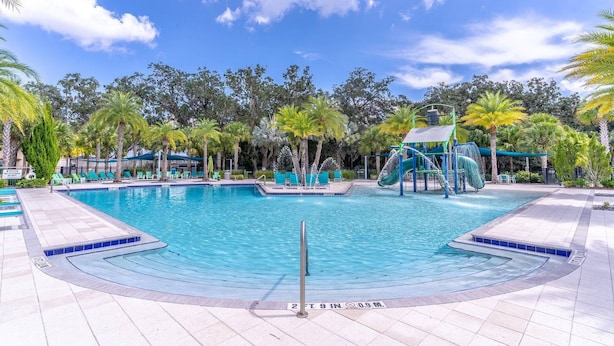 A swimming pool with a slide, surrounded by palm trees and lounge chairs.