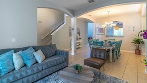 A modern living room with a sofa, coffee table, and dining area with chairs and a chandelier.