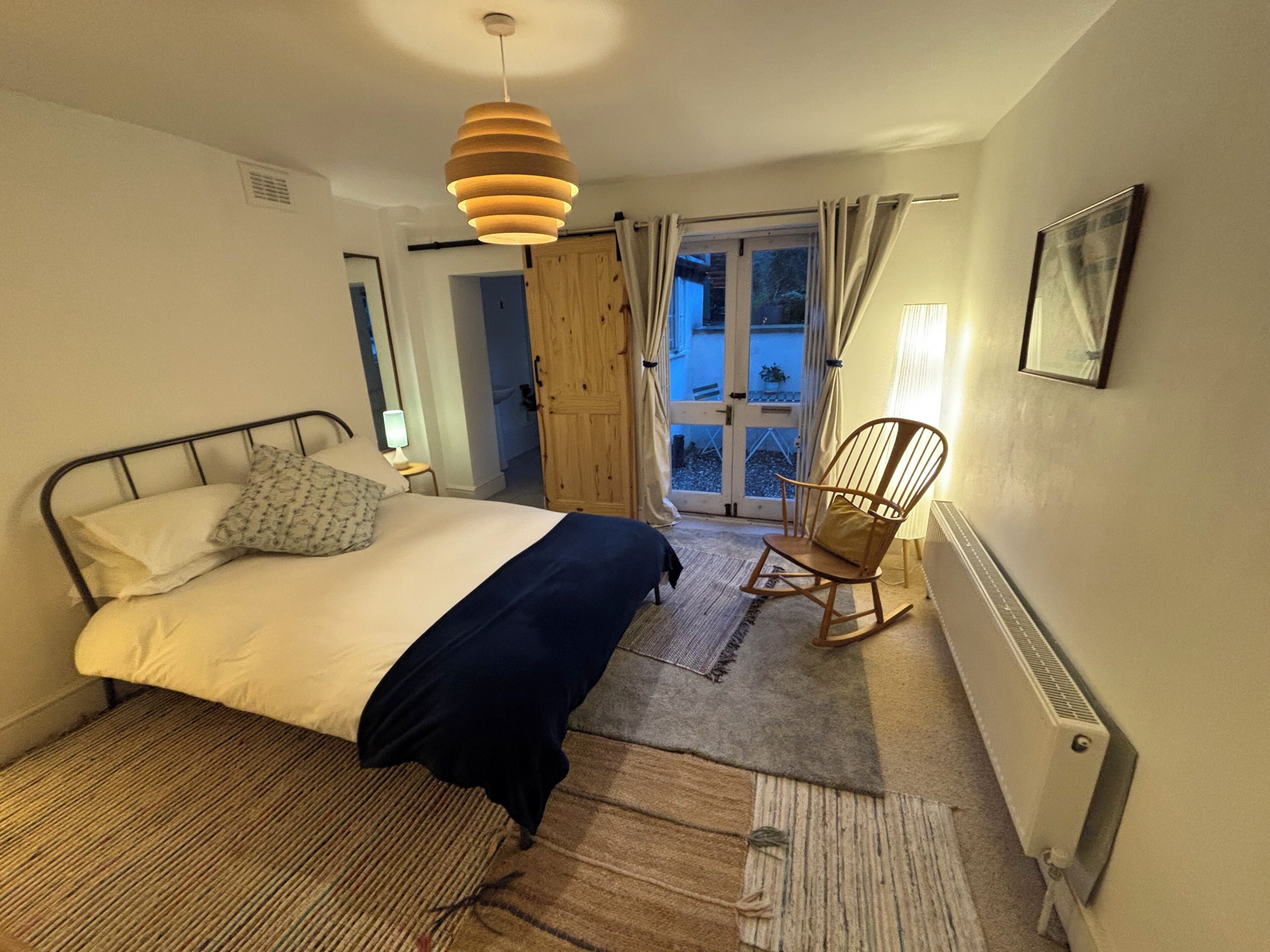 A bedroom with a bed, a rocking chair, a door leading outside, and a radiator.