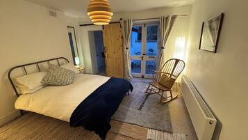 A bedroom with a bed, a rocking chair, a door leading outside, and a radiator.