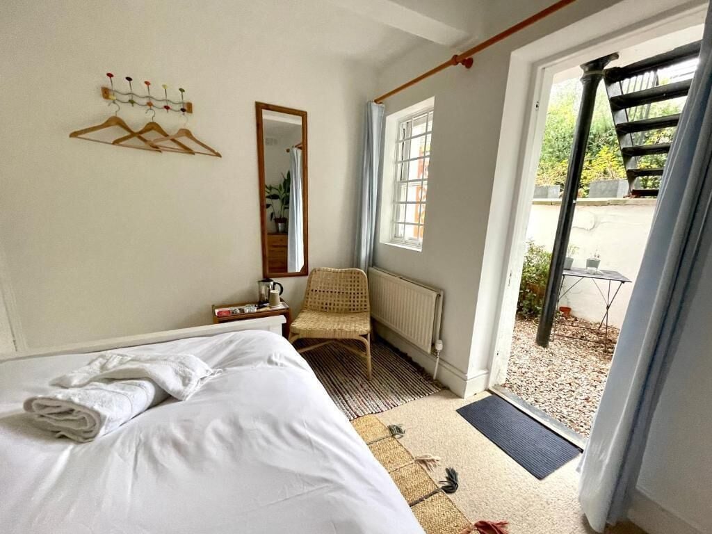 A bedroom with a bed, a chair, a radiator, a window, and a door leading to an outdoor area.