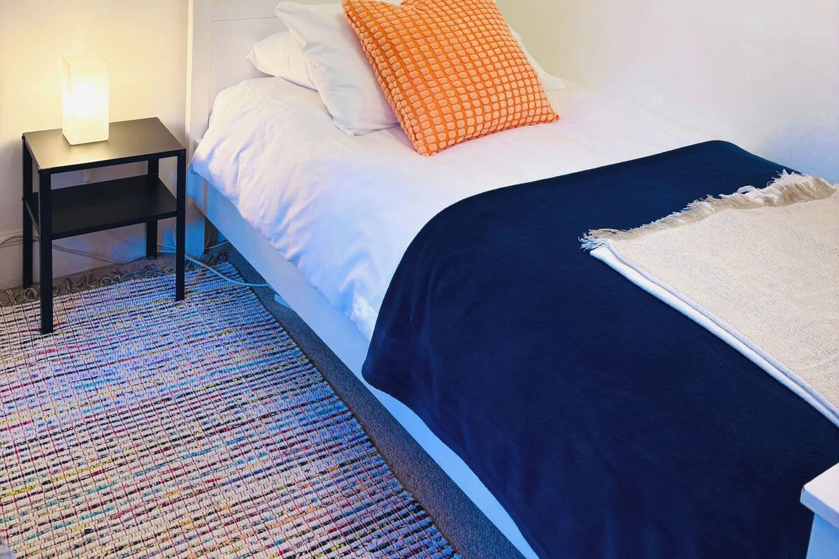 A bedroom with a bed, a nightstand, a framed poster, and a patterned rug.