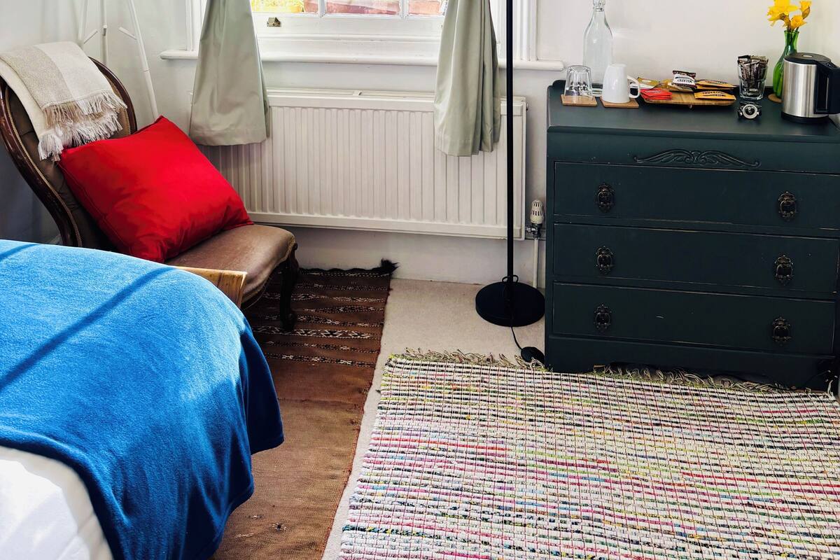 A bedroom with a bed, a chair, a dresser, a mirror, and a window with curtains.