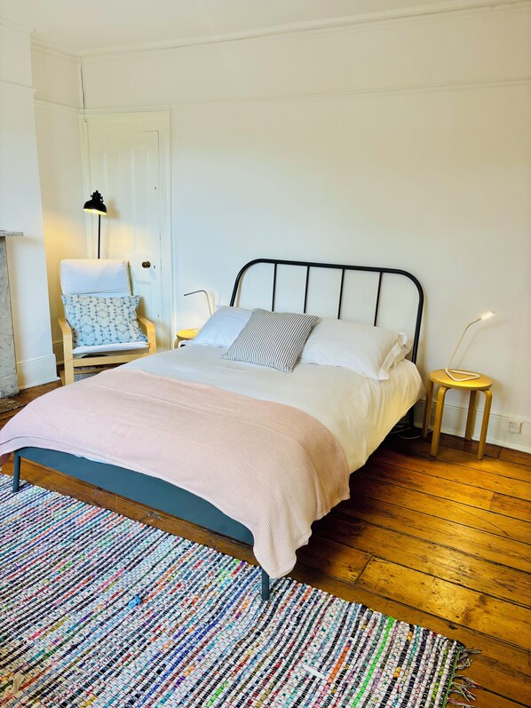 A bed with a headboard, a bedside table, a chair, a lamp, and a patterned rug. - Central Victorian House (London)
