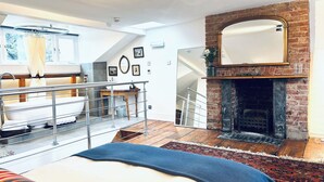 A modern bedroom with a large bed, a bathroom with a bathtub, a fireplace, and a view of a staircase. - Central Victorian House (London)