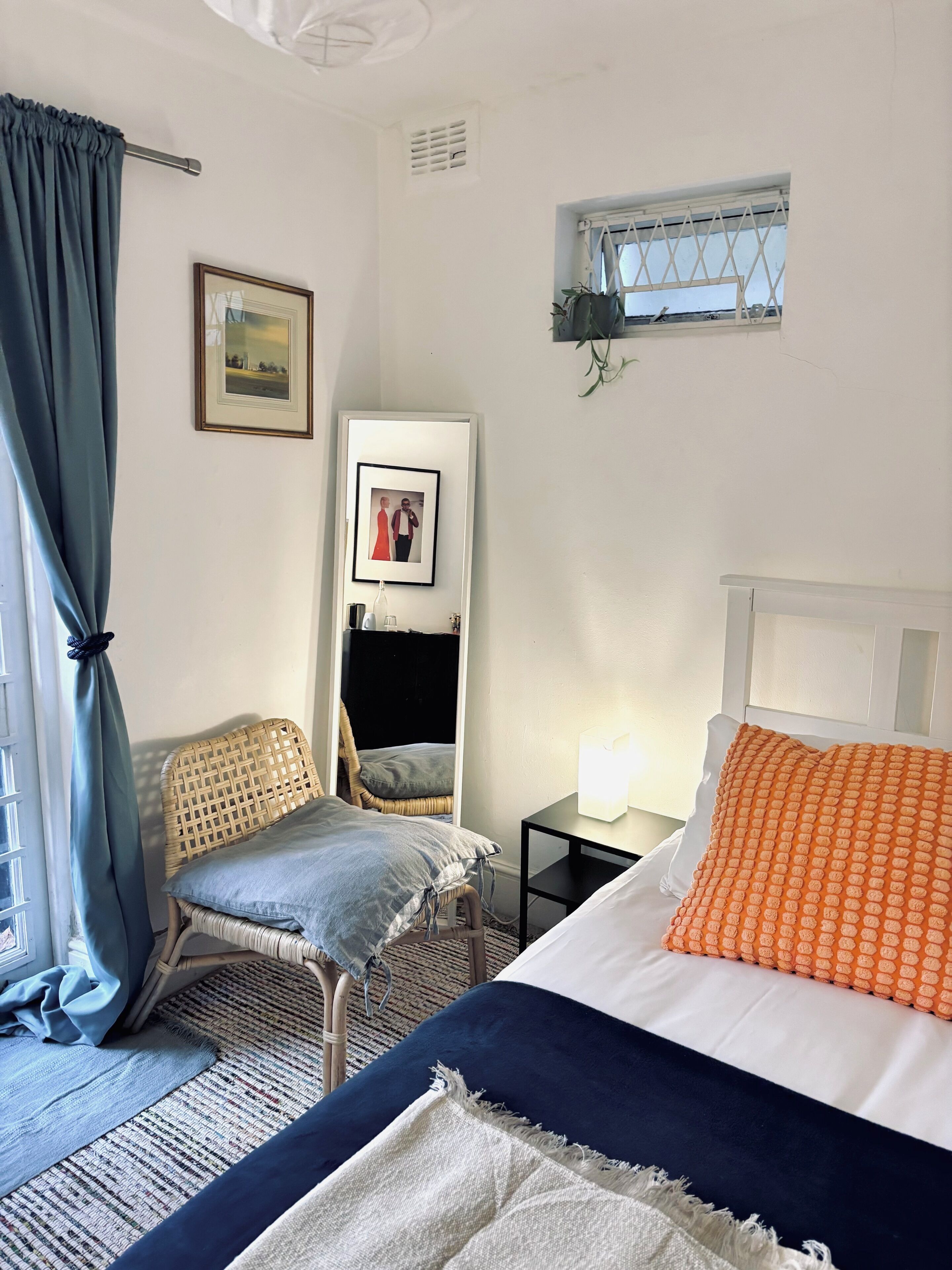 A bedroom with a bed, a chair, a bedside table, a mirror, and a window.
