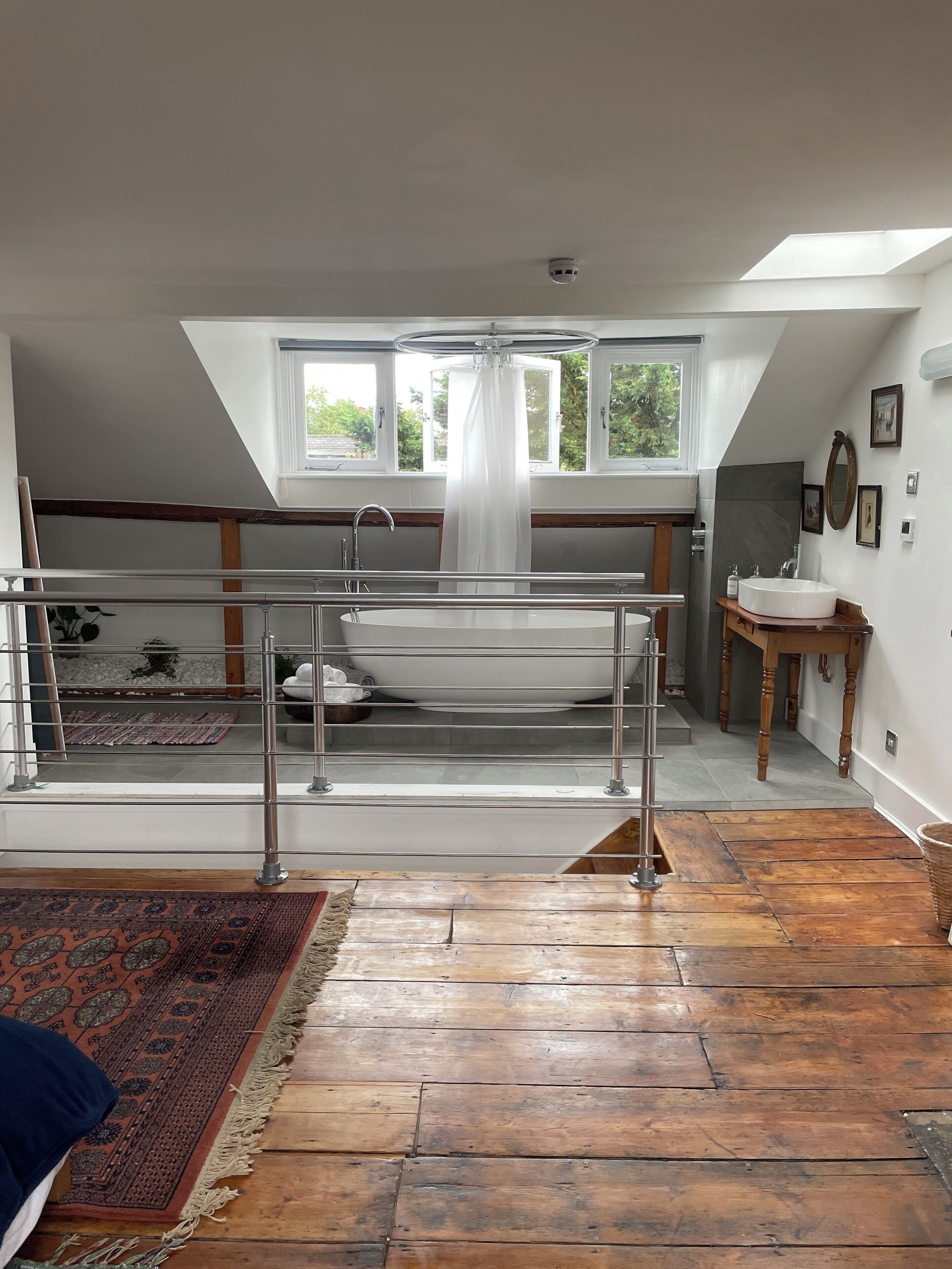 A spacious loft bedroom with a skylight, a large window, a skylight, a bathtub, and a wooden floor.