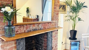 A brick fireplace with a wooden mantel, a mirror, a vase with flowers, a potted plant, and a small table with a kettle. - Central Victorian House (London)