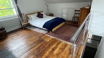 A bedroom with a wooden floor, a bed with a blue blanket, a window with curtains, and a ceiling fan.