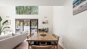 Un comedor moderno con una mesa y sillas de madera, un sofá y vistas al exterior a través de un ventanal.