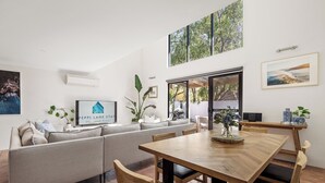 Una sala de estar moderna con un sofá, una mesa de comedor y sillas. Hay un televisor, una planta y un cuadro en la pared.