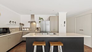 A modern kitchen with a large island, two bar stools, a microwave, a toaster, and a sink. - Peppi Lane Stay - Margaret River  (Margaret River)