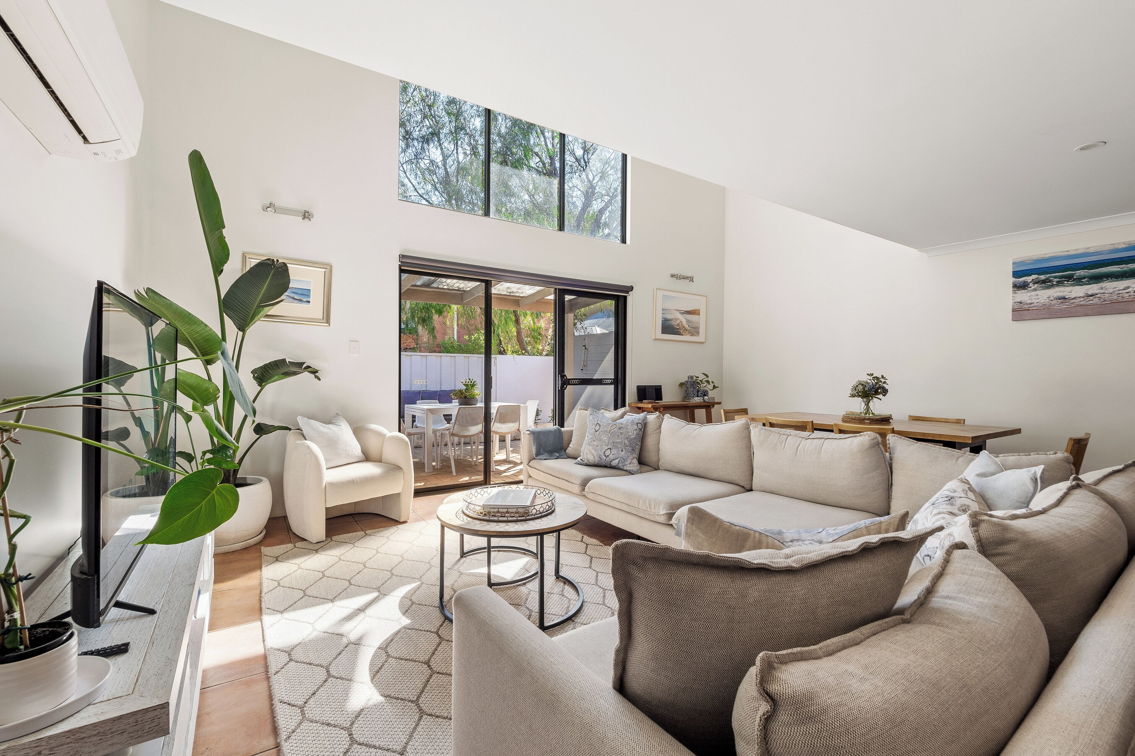 A spacious living room with a large window, a sofa set, a coffee table, and a potted plant.