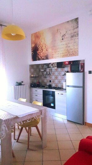 A compact kitchen with a dining area, a yellow pendant light, and a large abstract painting above the counter. - CASA MAFALDA Near the train station - historic center - private on-site parking (Imola)